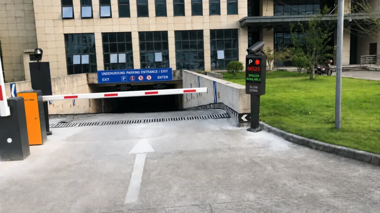 License plate recognition parking system at an underground garage entrance with barrier gate, LPR camera, and digital parking availability sign.